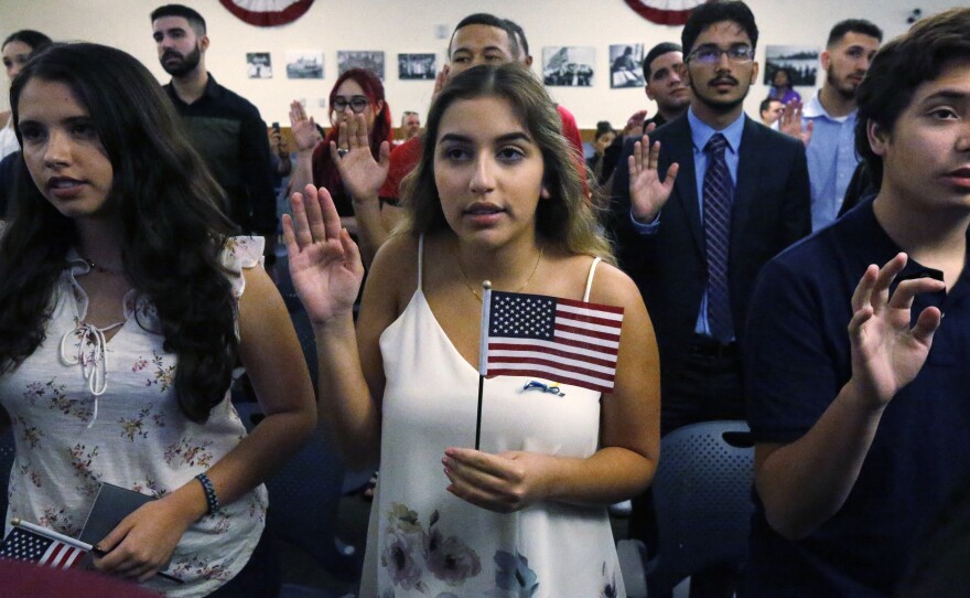 Ericka Ames, center, of Nicaragua recites the Oath of Allegiance during a naturalization ceremony at the U.S. Citizenship and Immigration Services in Miami. The backlog of citizenship applications has increased dramatically under the Trump administration.