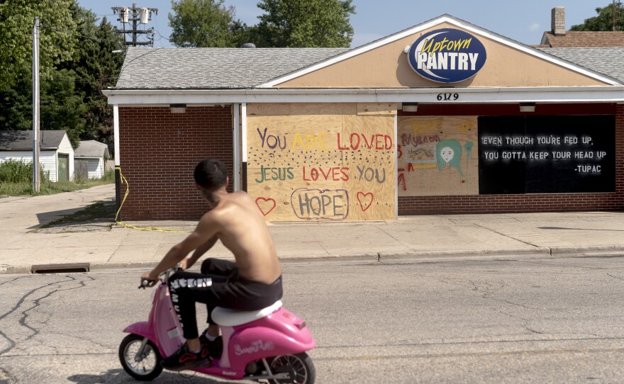 A man rides a scooter past a boarded-up Uptown Pantry in Kenosha, WI.