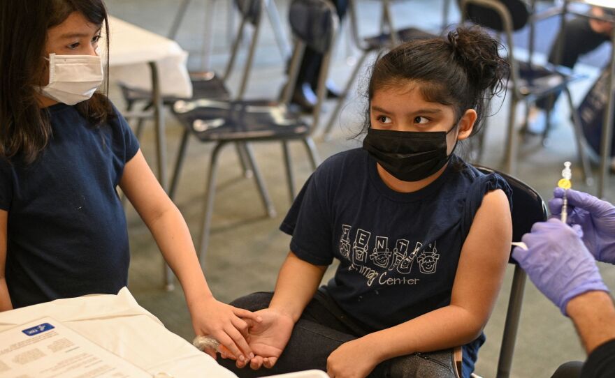 Pfizer will submit new data to the FDA this week about trials of its vaccine for kids younger than 5 years old. Here, a girl holds her sister's hand as a nurse prepares to administer the COVID-19 vaccine at a vaccination clinic in Los Angeles. Kids 5 and older have been eligible for the vaccine since last November.