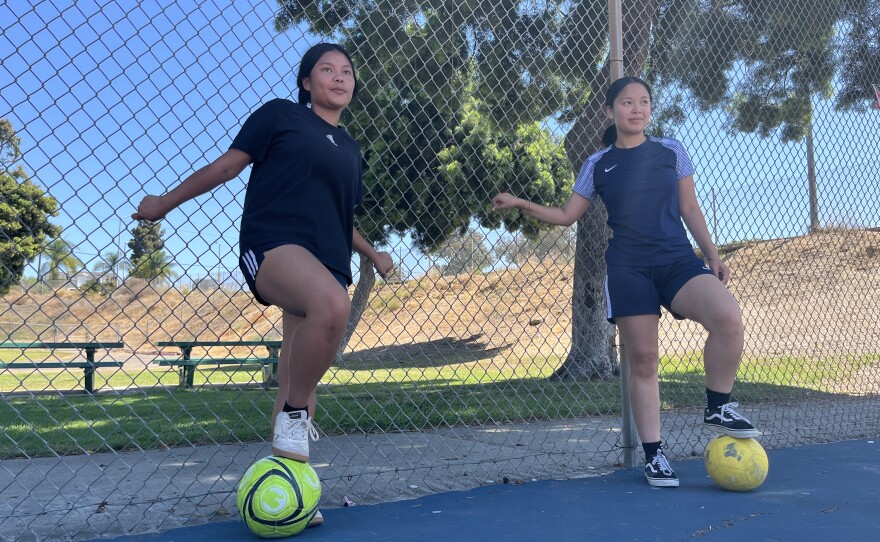 Cousins Venus (left) and July Wah (right) lean against the fences of Colina Del Sol Park's basketball courts with soccer balls at their feet, July 10, 2025.