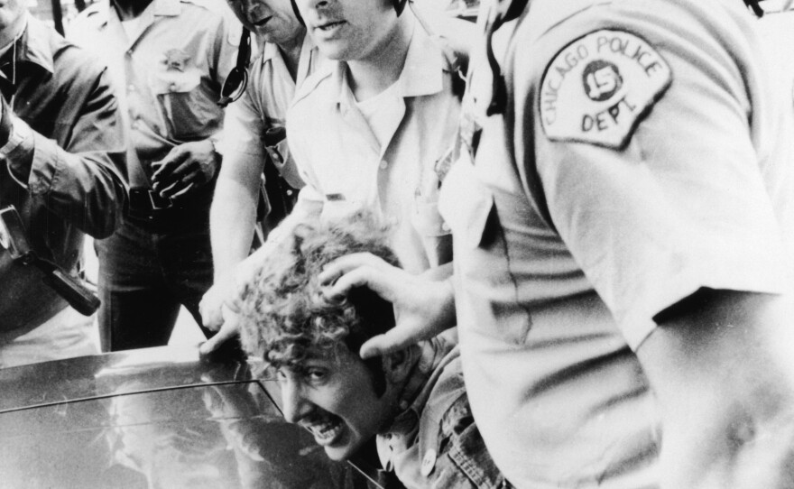 Officers from the Chicago Police Department push a protester's head against the hood of a car after he climbed onto a wooden barricade near the Democratic National Convention and waved a Vietcong flag during anti-Vietnam War demonstrations in 1968.