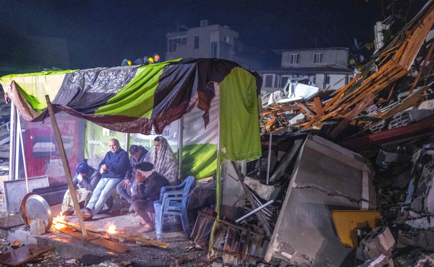 People take rest next to bonfire in the rubble in Hatay, Turkey after a 7.8-magnitude earthquake struck the country's southeast on Monday.