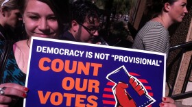 A young woman holds up a sign at the Maricopa County Department of Elections office.