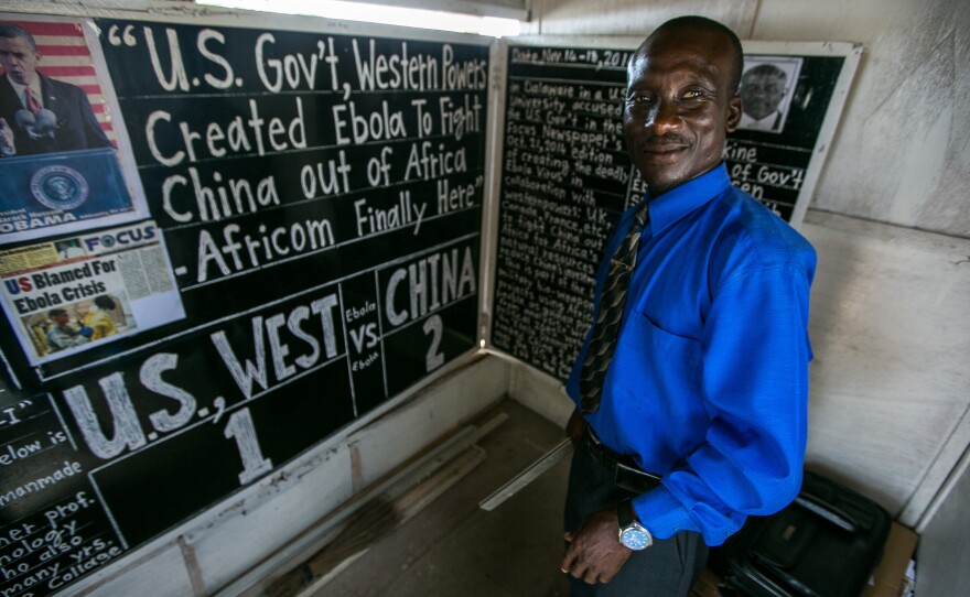 Alfred Sirleaf stands inside his newsroom: a plywood hut behind the Daily Talk blackboard. He composes a new edition every three days or so.