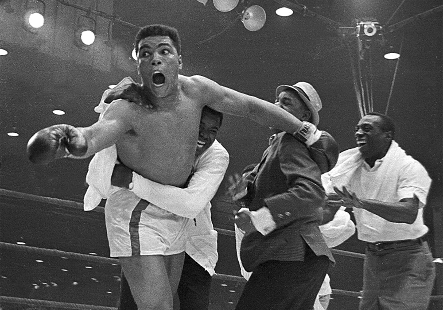 Cassius Clay's handlers hold him back after he is announced the new heavyweight champion of the world after knocking out Sonny Liston. Bundini Brown embraces Ali. Luis Sarria runs to the group in a smile on the right. Miami, Fla. Feb. 25, 1965.