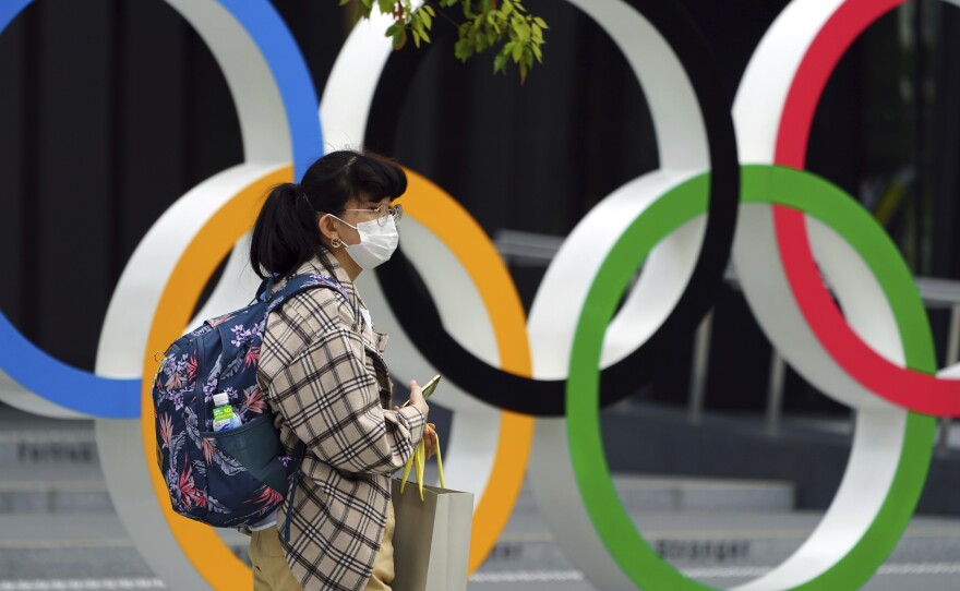 A woman wearing a protective mask to help curb the spread of the coronavirus walks in front of he Olympic Rings on Tuesday in Tokyo. North Korea says it will not attend the games over COVID-19 fears.