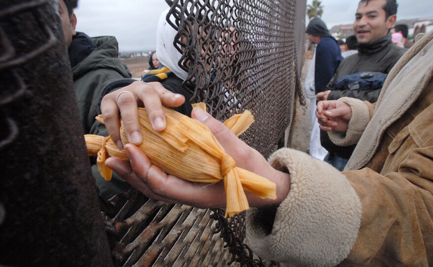 Fandango Fronterizo passing a tamale through the American/Mexican border fence.