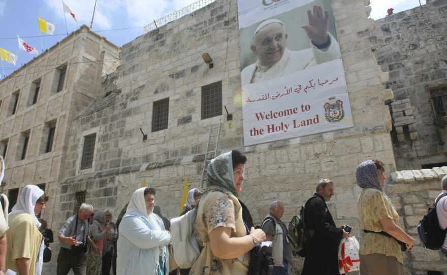 Tourists walk past a poster of Pope Francis hanging on the Church of the Nativity in the West Bank town of Bethlehem on Monday. Pope Francis' trip to the Mideast later this week will commemorate the 50th anniversary of a historic rapprochement between Catholics and Orthodox, who split nearly 1,000 years ago.