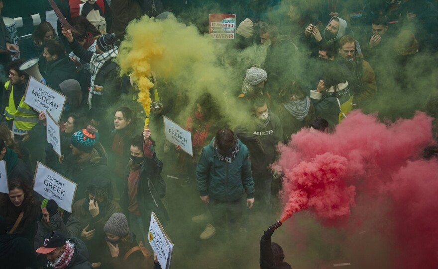 Protesters brandish colored flares during a rally Thursday in Paris as part of one of France's largest nationwide strikes in years. President Emmanuel Macron's intended changes to the pension system are facing resistance from transportation workers, teachers, students, airline workers and other union employees.