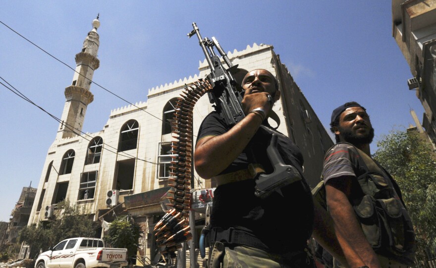 Forces loyal to Syria's President Bashar Assad carry their weapons as they walk along a street in Mleiha, near the Damascus airport, during a tour organized by the Syrian government on Aug. 15.