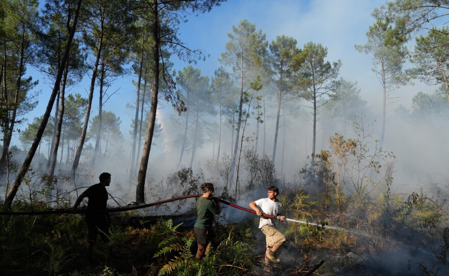 A group holds a firehose and tries to suppress a fire near Lacanau, as wildfires rage outside Bordeaux, France, Monday, July 27, 2026.