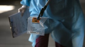 A physician assistant carries a nasal swab sample using a grabber at a COVID-19 drive-through testing site set up at the Anaheim Convention Center in Anaheim, Calif., Thursday, July 16, 2020.