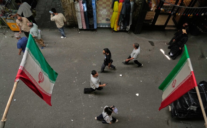 People walk as Iranian flags hang in the Grand Bazaar in Tehran, Sunday, May 3, 2026.