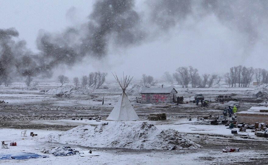 Snow falls on the Oceti Sakowin camp on Wednesday as structures smolder.