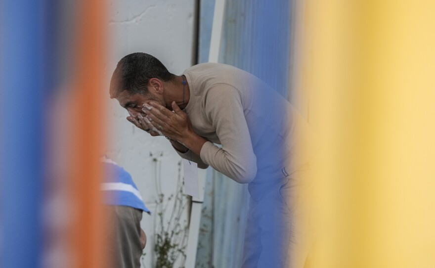 A survivors of a shipwreck washes his face outside a warehouse at the port in Kalamata town, about 240 kilometers (150miles) southwest of Athens on Wednesday, June 14, 2023.