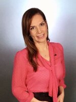 Woman smiling at camera with dark, long hair wearing a pink shirt.