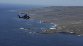 A Marine Corps Ah-1Z SuperCobra attack helicopter flies from the left toward the western rocky shore of San Clemente Island.
