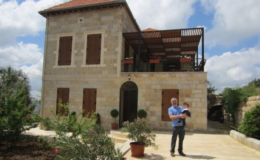 Shadid holds his son in front of the family home he spent years renovating in Marjayoun, Lebanon.