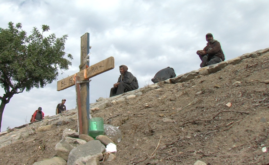 Migrants sit behind a memorial cross erected for a friend killed on the highway, Dec. 15, 2015.