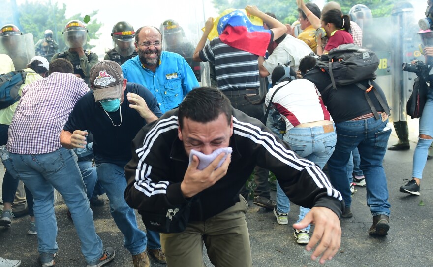 A demonstrator protects his mouth with a cloth as riot police advance on protesters on Wednesday. Security forces fired tear gas and water cannons at protesters during the Caracas rally, while protesters often returned fire with rocks and other objects.