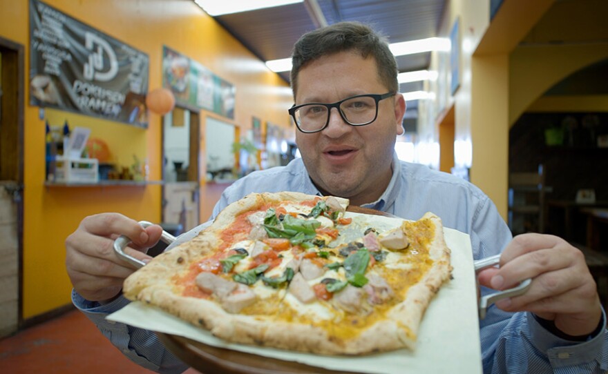 Host Jorge Meraz holds up a traditional Italian pizza from ABC Pizza in Rosarito, Mexico.