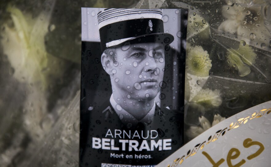 A photo of Lt. Col. Arnaud Beltrame rests on a bunch of flowers at the main gate of the police headquarters in Carcassonne, France. On Sunday, a man was arrested on charges of apologizing for terrorism after seemingly praising Beltrame's death on social media.