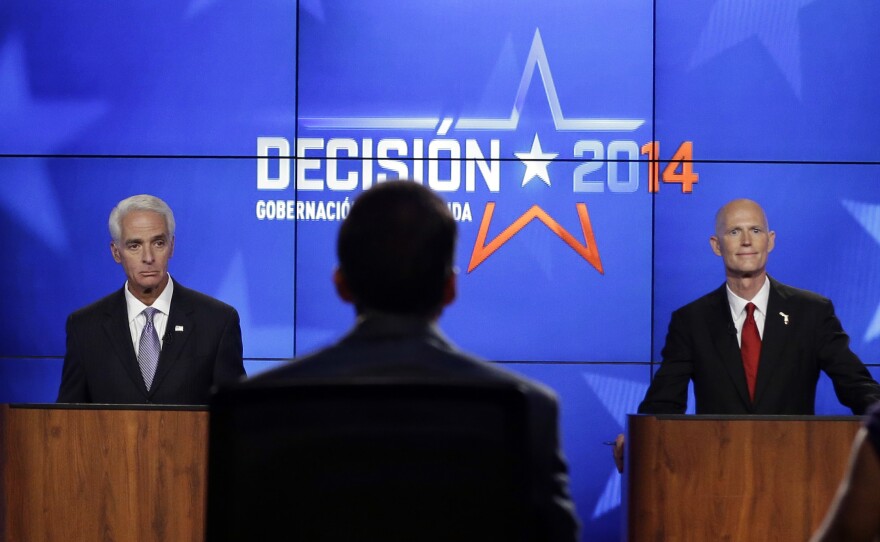 Democrat Charlie Crist, a former Republican governor of Florida (left), and Rick Scott, the current Republican governor of Florida, listen to the moderators during a gubernatorial debate on Friday. The two are facing off in a tight race that's fueling a barrage of negative campaign ads.