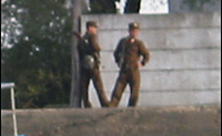 Two North Korean People’s Army soldiers in brown fatigues stand on the riverfront near a shipbuilding factory in Sinuiju.