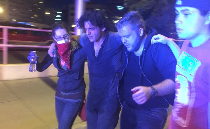 Protesters help a fellow demonstrator who was affected by the smoke and pepper spray reportedly used by police to disperse the crowd outside Tuesday's rally for Republican presidential candidate Donald Trump in Albuquerque, N.M.