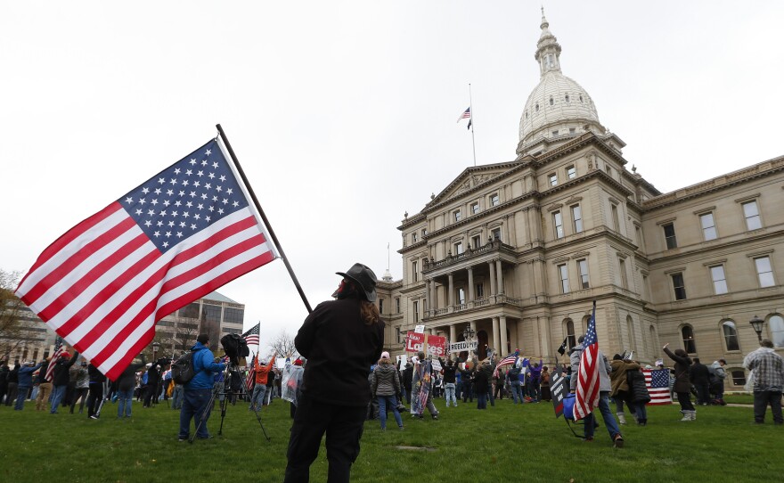 A protester holds an American flag on the lawn of the Michigan Capitol on April 30, 2020. Lawmakers in Shiawassee County are vowing to return $65,000 in bonuses they gave themselves using federal coronavirus relief funds.