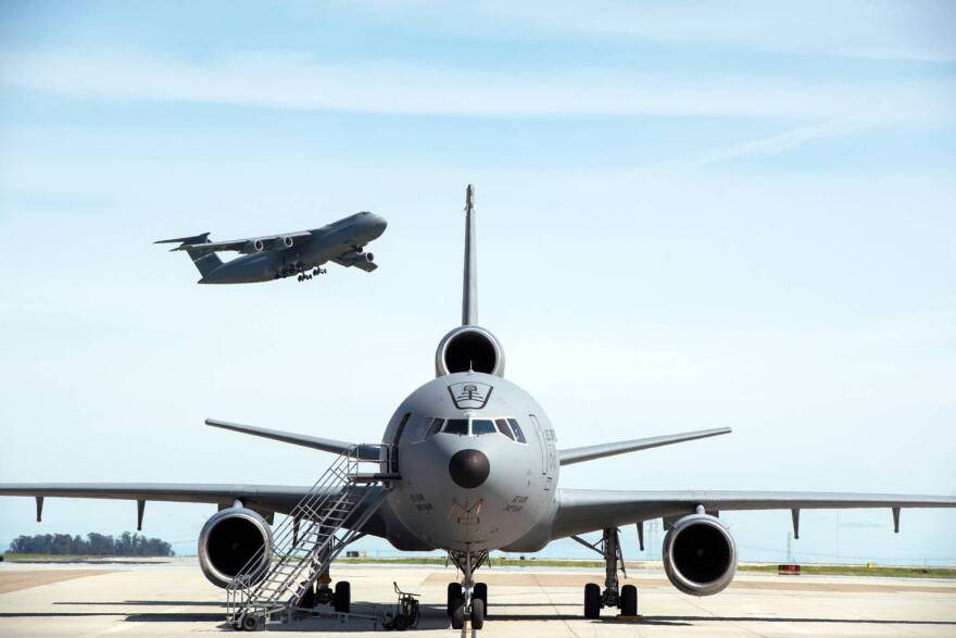 A KC-10 Extender is parked on the ramp as a C-5M Super Galaxy takes off at Travis Air Force Base, California, March 16, 2017.
