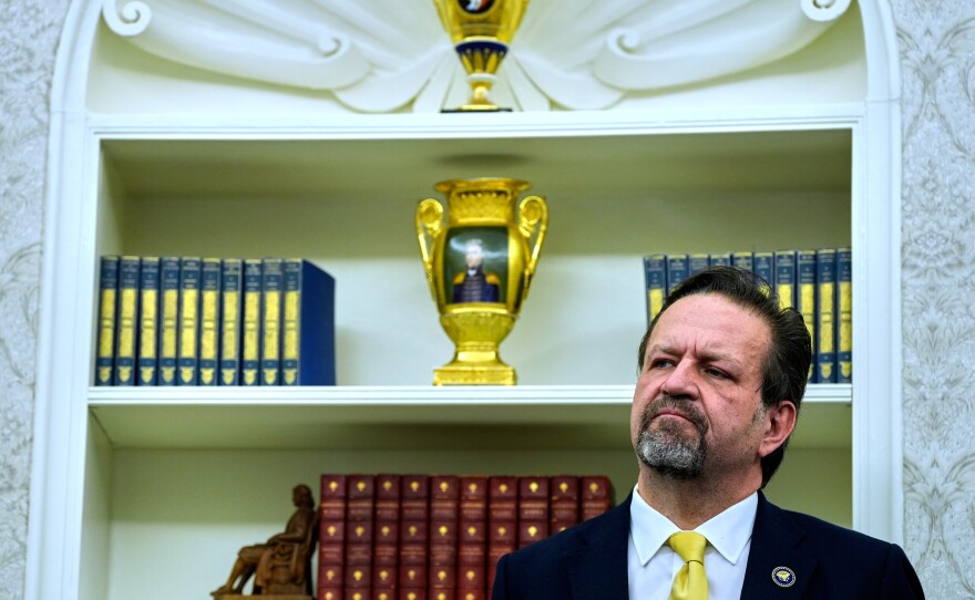 Sebastian Gorka listens as President Donald Trump speaks with reporters after signing executive orders in the Oval Office of the White House, April 23, 2025, in Washington.