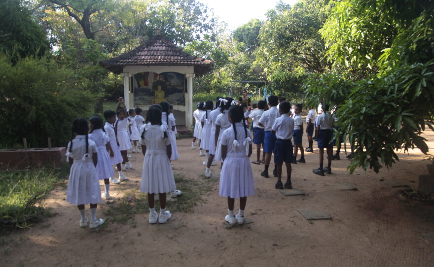 Children chant Buddhist prayers at a local public school in the town of Sigriya in central Sri Lanka as they wait for Nilanthi Kumari to ladle out a fresh hot meal for their lunch.   Kumari says the government pays her about 35 cents per meal — but with rising costs caused by the Mideast war, she's barely breaking even — and she's thinking about walking away from this job, which keeps vulnerable children nourished.