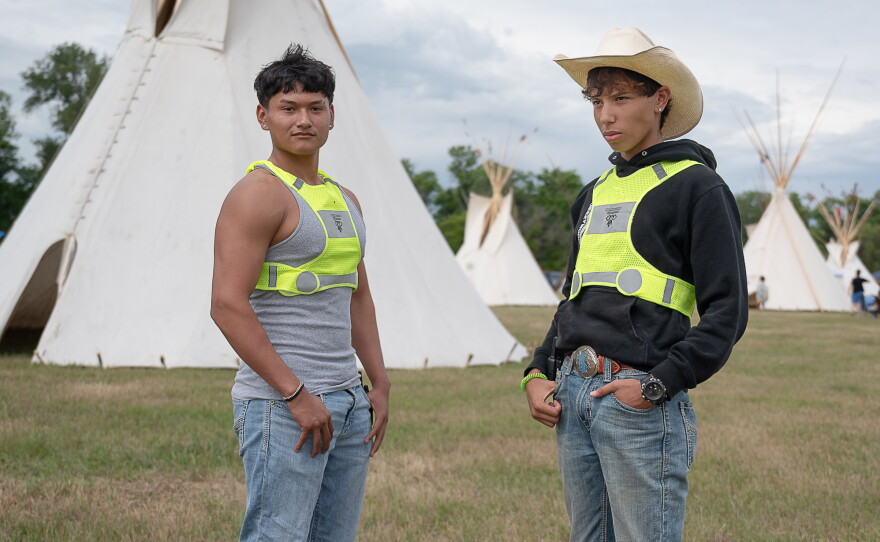 Champion Marquez and his friend Elijah Wallowing pose in front of a tipi in the encampment.