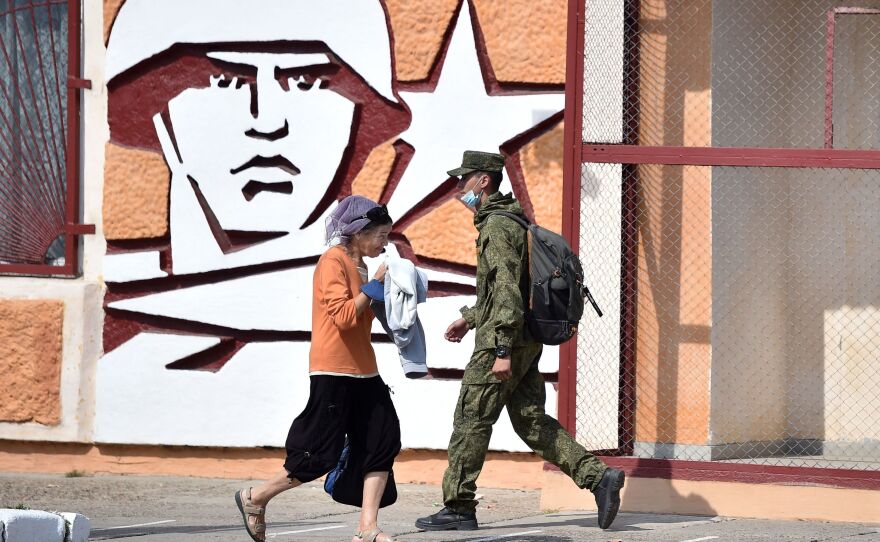 A soldier and a woman walk past the headquarters for Russian troops in September 2021 in the town of Tiraspol, in Trans-Dniester, a pro-Russian region that declared independence from Moldova but is internationally unrecognized. Russia has stationed 1,500 soldiers in the area.