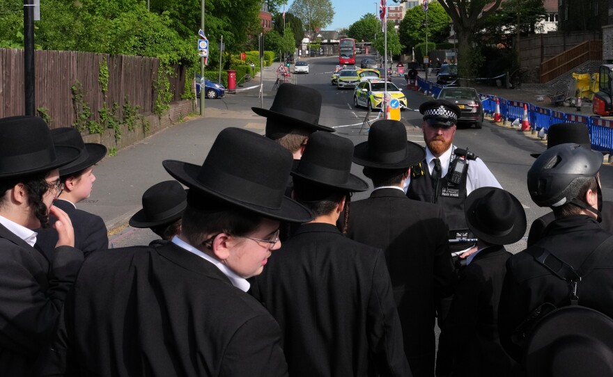 Members of the community watch as forensic officers search the area after two people were stabbed in the Golders Green neighborhood, that has a large Jewish community, in London, Wednesday.