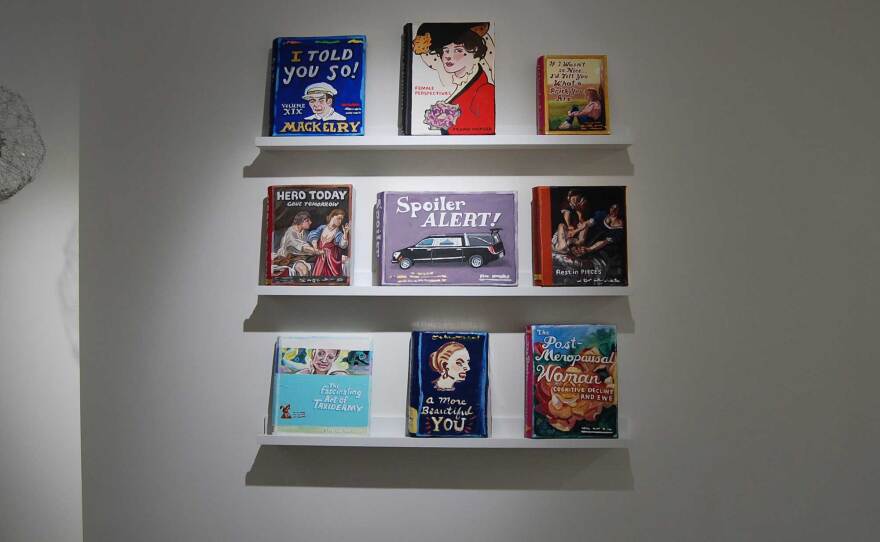 Bookshelves with papier-mâché books with fictionalized titles are part of Jean Lowe's "POW!" exhibition on view now at Quint ONE.