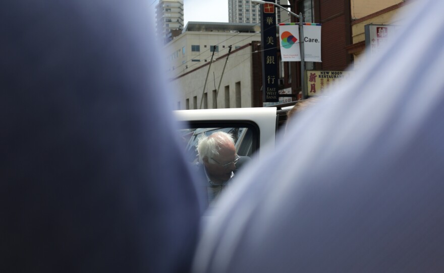 Sanders enters a vehicle in his motorcade, disappearing behind the sea of supporters still standing on the street.