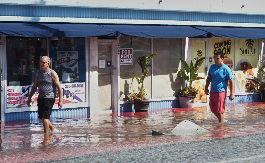 Pedestrians walk through a flooded street caused by king tides and heavy rain Wednesday, Oct. 28, 2026, in North Bay Village, Fla.
