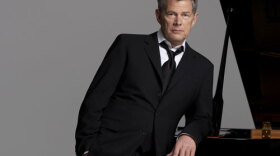 Promotional photo of the legendary songwriter/producer David Foster standing next to a piano. 