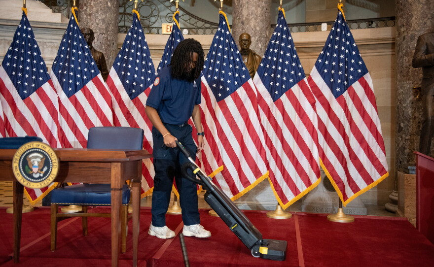 A worker vacuums the stage in Statuary Hall, in the Capitol, where President Trump was scheduled to sign a bipartisan housing bill on Wednesday before he abruptly cancelled the signing.