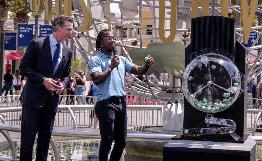 California Governor Gavin Newsom, left, looks on as Access Hollywood personality Scott Evans draws a ball with a winning number during the Vax for the Win lottery contest at Universal Studios in Universal City, Calif., Tuesday, June 15, 2021.