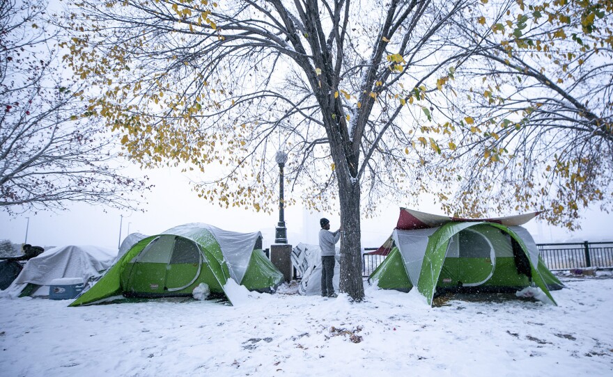 A man secures a tent in an encampment on Denver's Zuni Street, where migrants who had stayed in a city-contracted motel relocated after they had to leave the facility. Oct. 28, 2023.