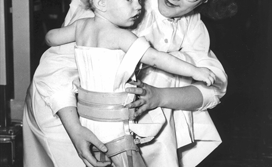 Nurse holds toddler, who is wearing leg and chest braces. (undated photo)