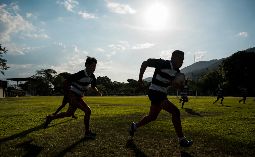 Rugby team players race after each other on the field.