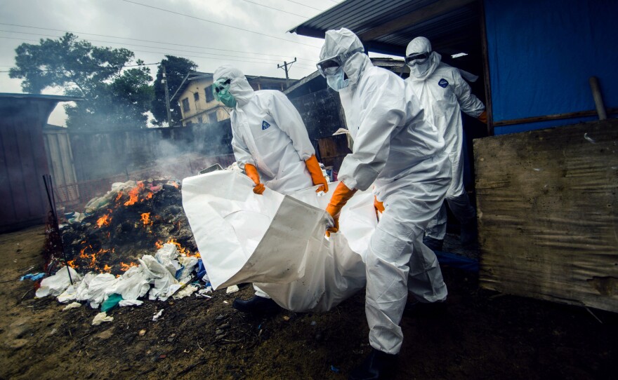 A burial team collects a body from the Ebola unit at JFK hospital in Monrovia. Protective suits are burnt in the background — a precautionary measure to prevent the spread of the virus.