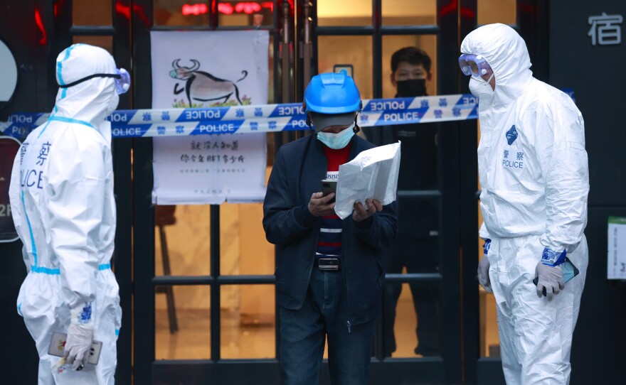 A delivery man walks by police officers with protective suit outside of a hotel in Shanghai, China, on March 15.