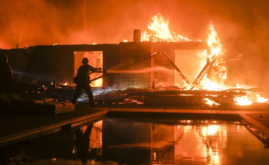 A firefighter battles the Woolsey Fire burning a home in Malibu, Calif. in November. Fire scientists are finding that homes most frequently burn from flying embers after the initial blaze has passed through.