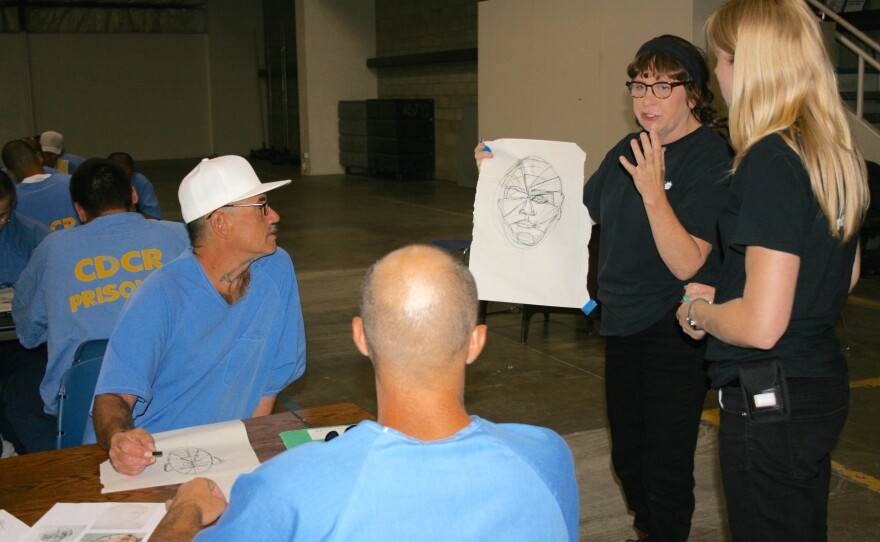 Project PAINT instructors (left to right) Kathleen Mitchell and Laura Pecenco discuss drawing techniques with inmates, Sept. 1, 2015.