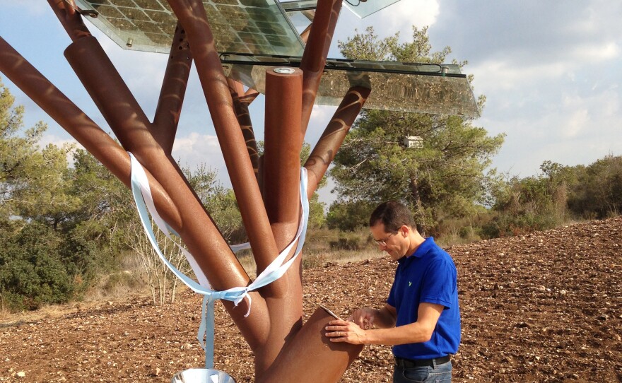 A man works beneath a solar tree in Israe. This tree has broad "leaves" that are standard solar panels. They can shade benches, as well as power electric and USB outlets, chill drinking fountain water and supply energy for wi-fi.
